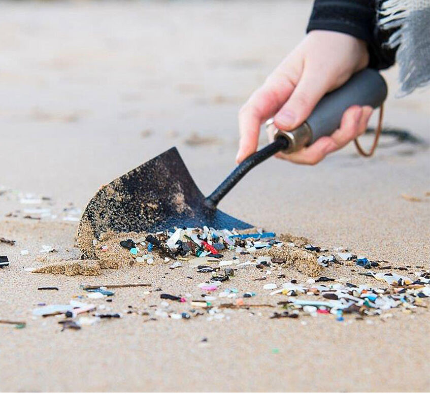 Hand picking up plastic garbage with shovel at sea